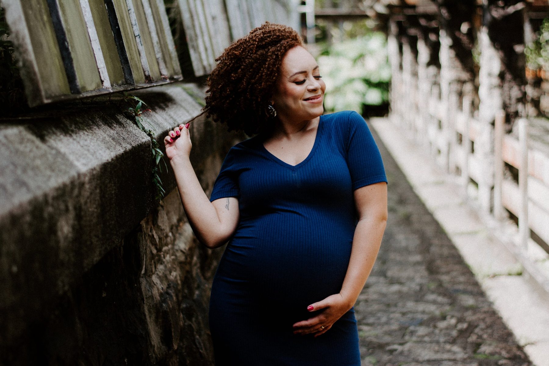 Gestante de vestido azul sorrindo de olhos fechados, com a mão na barriga