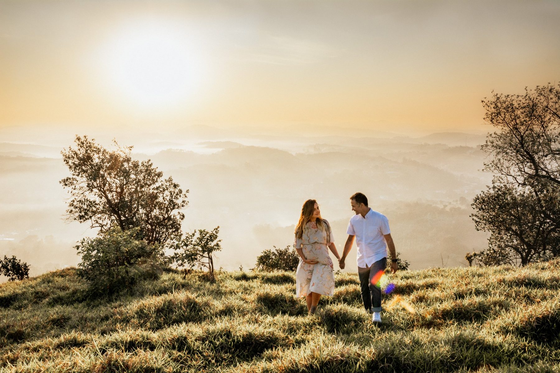 Casal de mãos dadas caminhando no alto de um morro ao nascer do sol
