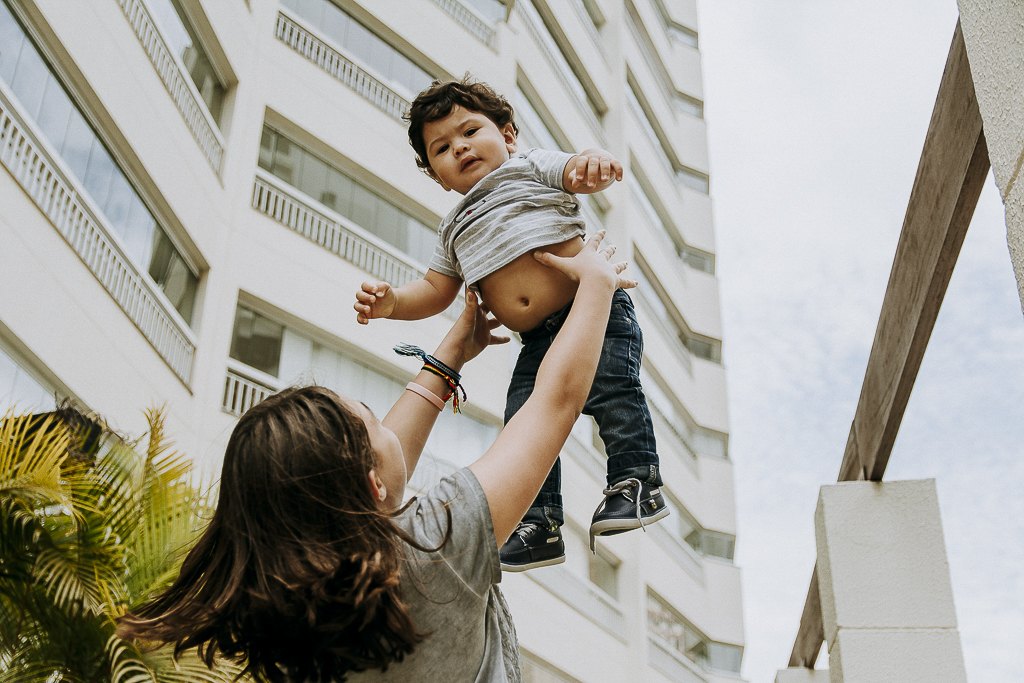 Irmã levantando o bebê para o alto, com prédios e céu ao fundo