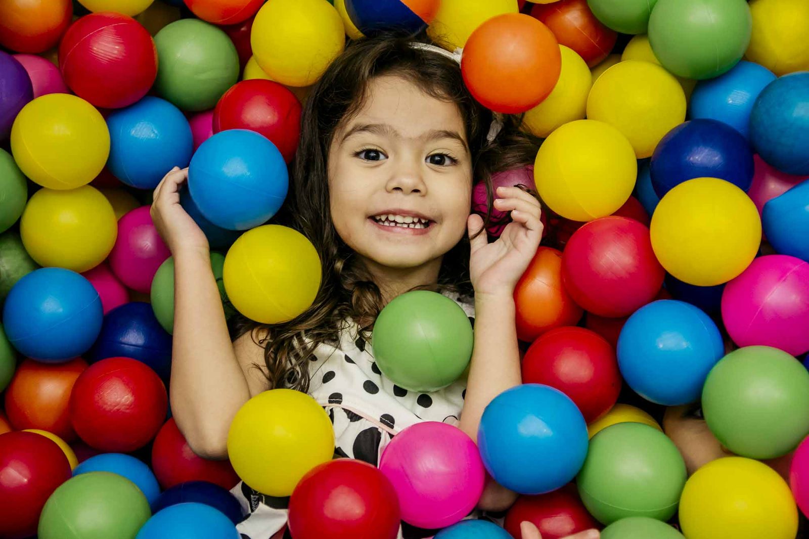 Menina sorrindo no meio de uma piscina de bolinhas coloridas