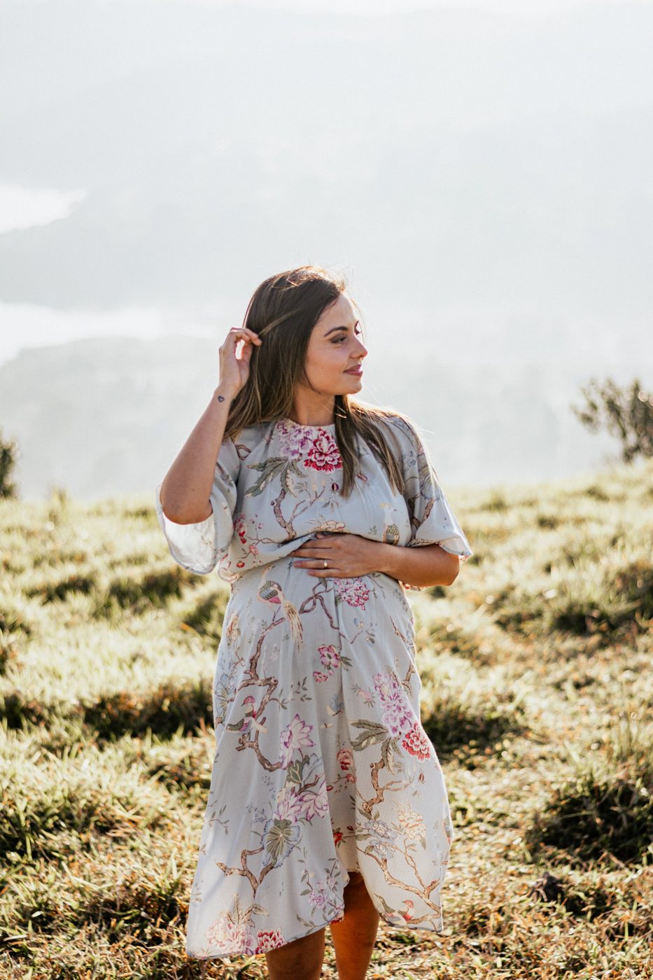 Gestante de vestido florido no campo, com a mão na barriga