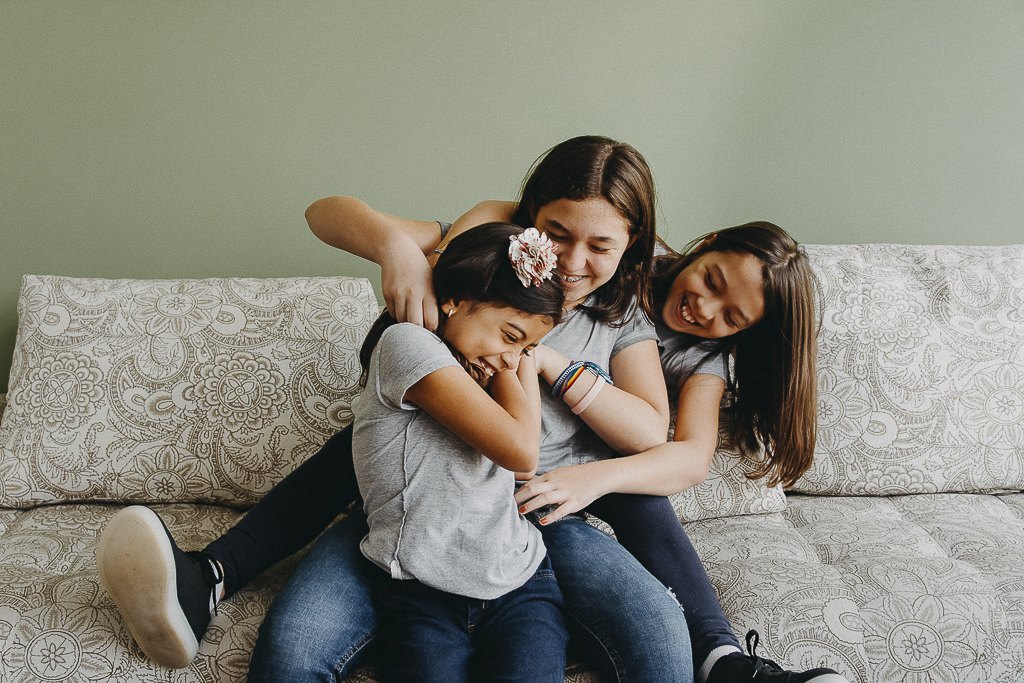 Três irmãs se abraçando e rindo no sofá